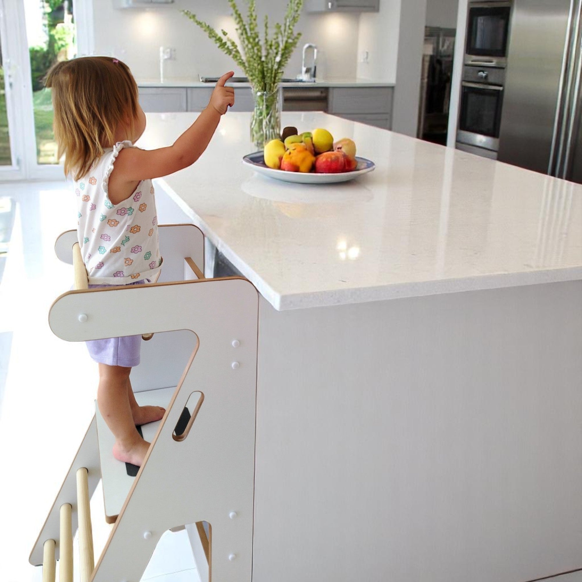 Niña usando la torre de aprendizaje Zalu en la cocina, de espaldas, junto a una isla