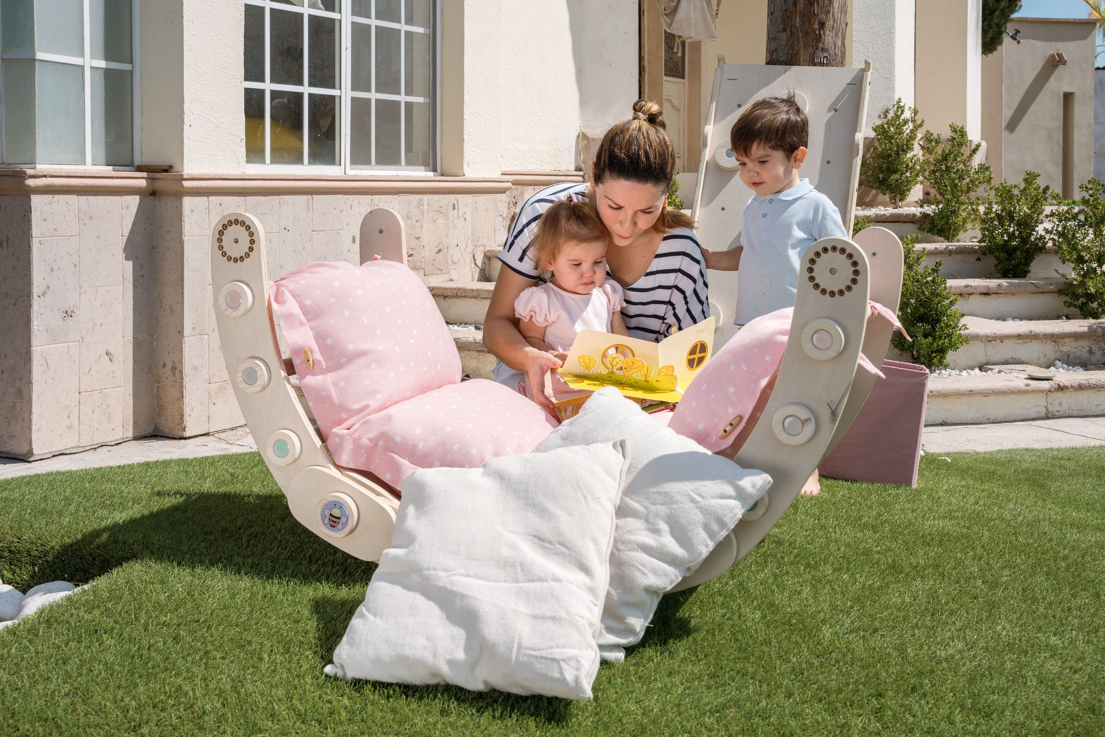 foto en familia de una mama leyendo a sus hijos en el jardin sobre un balancian de zalu