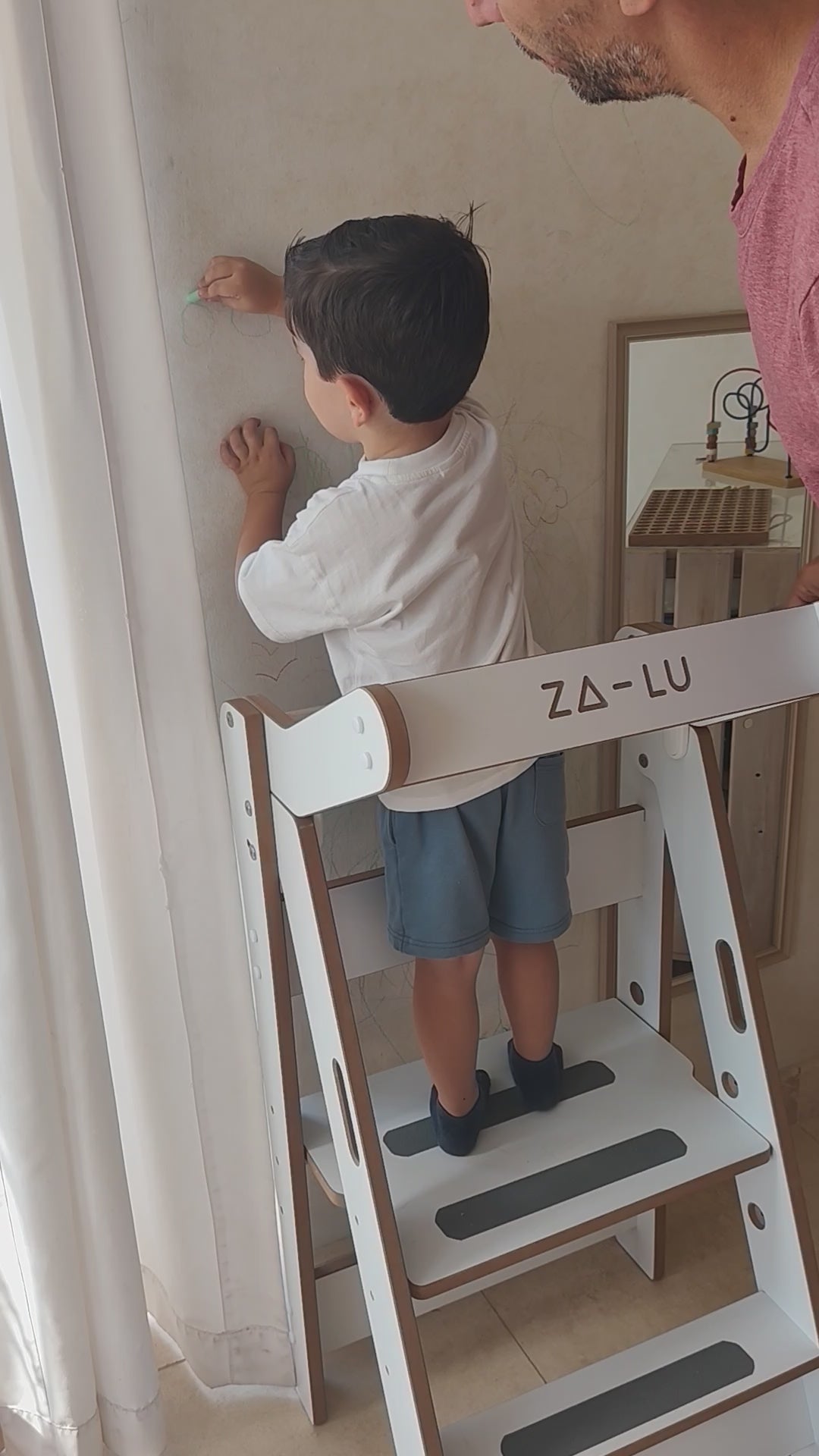niño sobre torre de aprendizaje montessori zalu pintando en una pared
