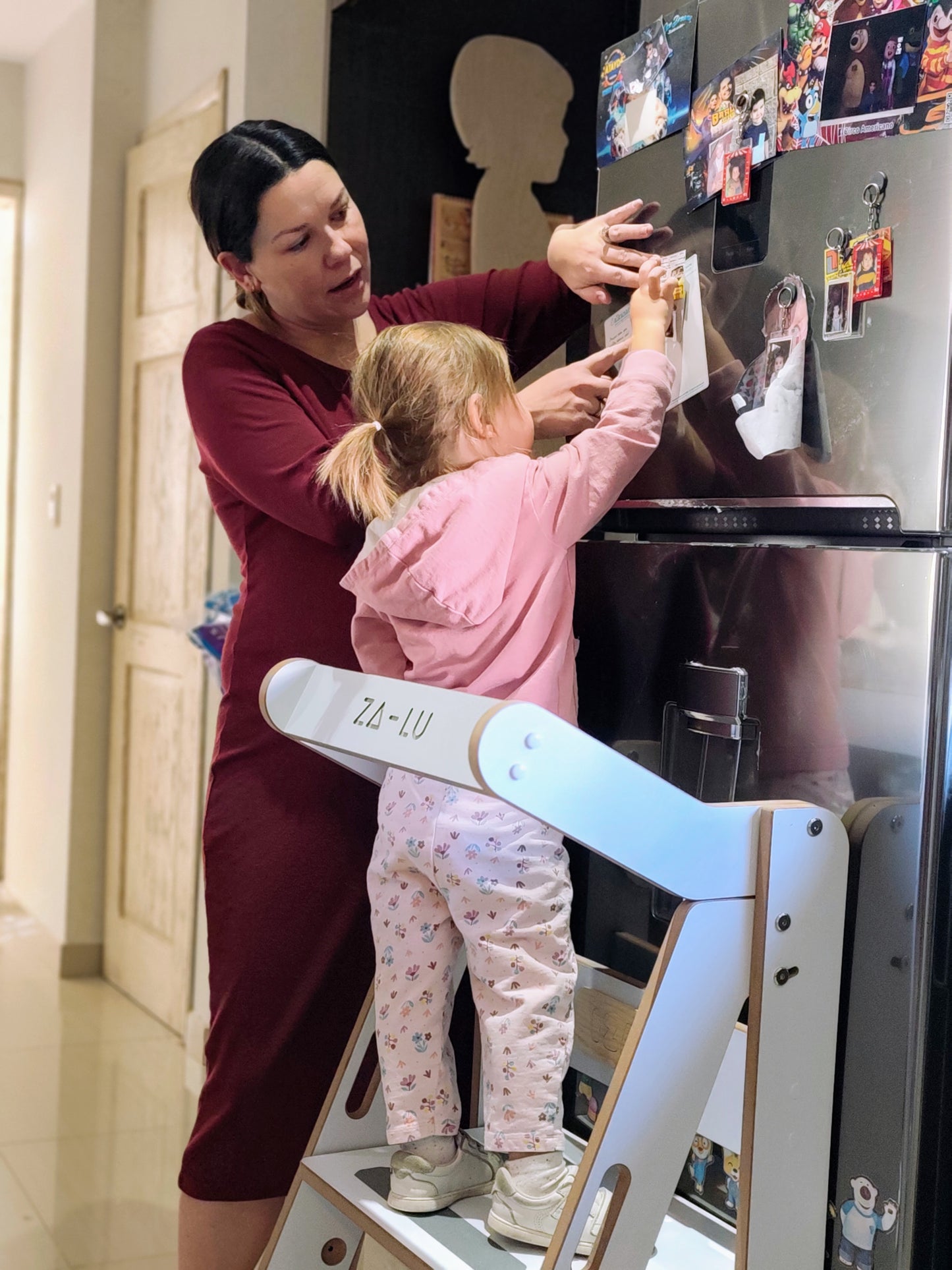 foto real de una mamá y su hija colocando un imán en la nevera con ayuda de la torre de aprendizaje zalu