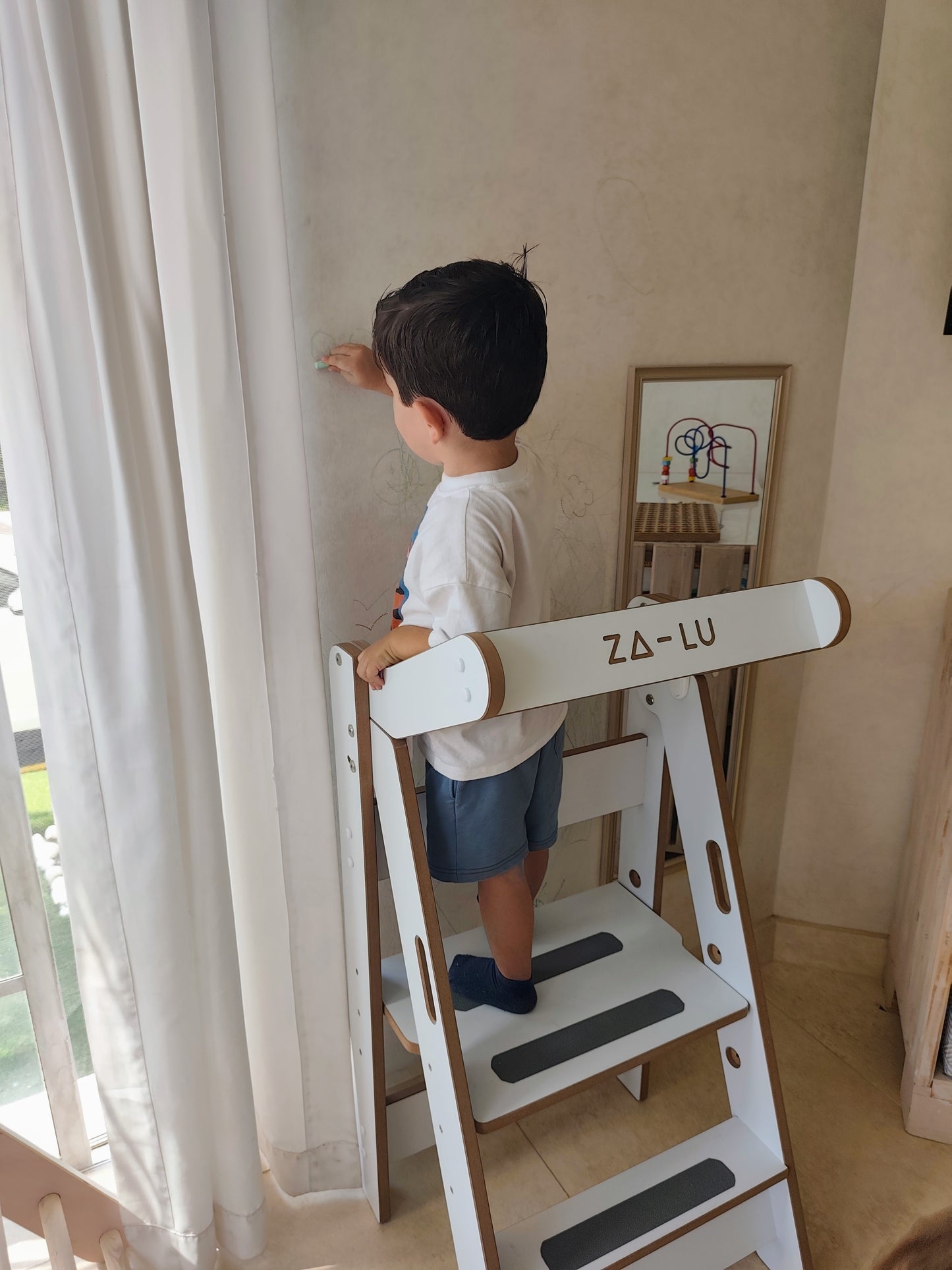 niño pintando en la pared subido en la torre de aprendizaje montessori zalu