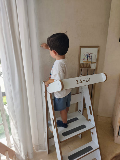 niño pintando en la pared subido en la torre de aprendizaje montessori zalu